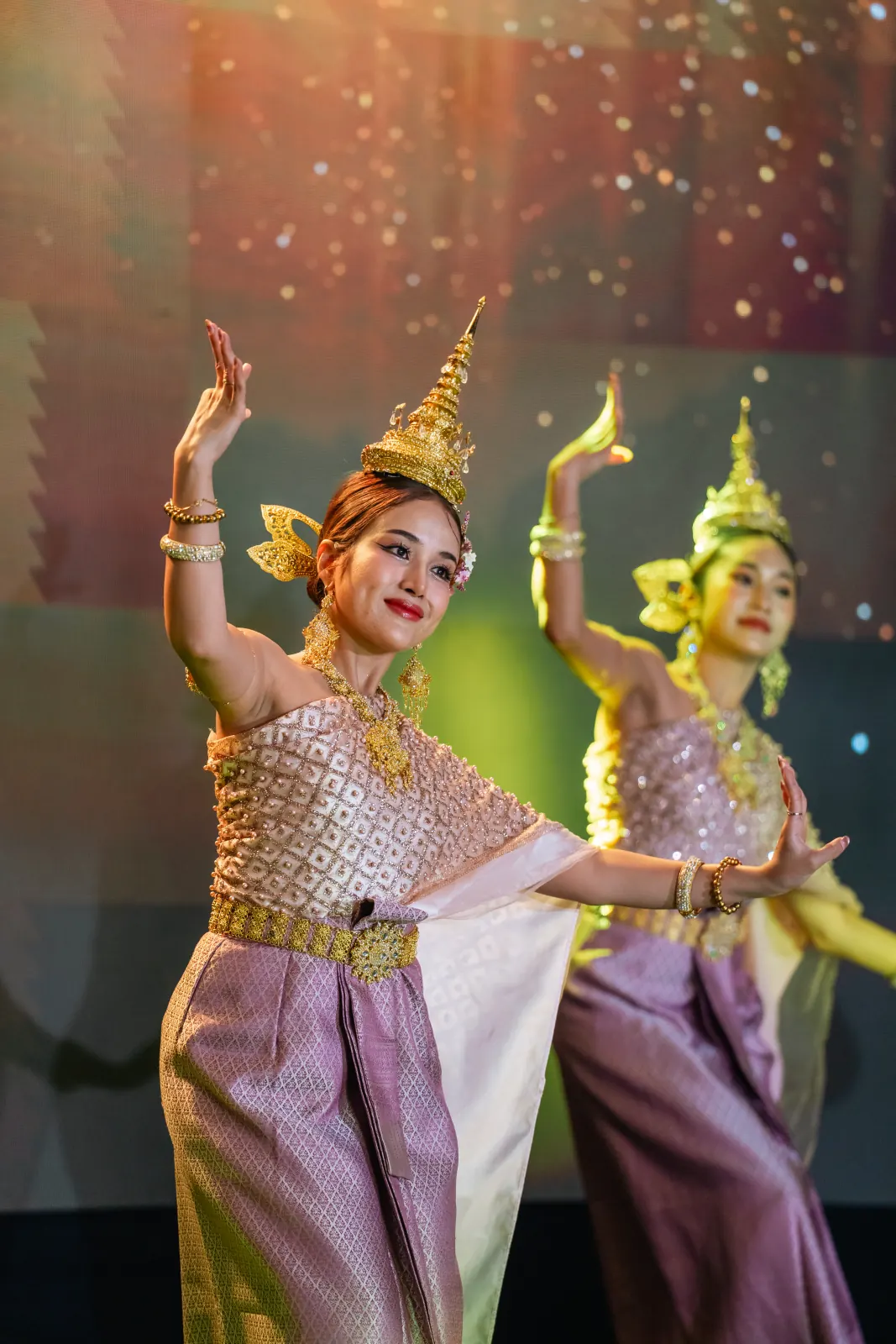 Two Thai dancers performing under warm stage lighting