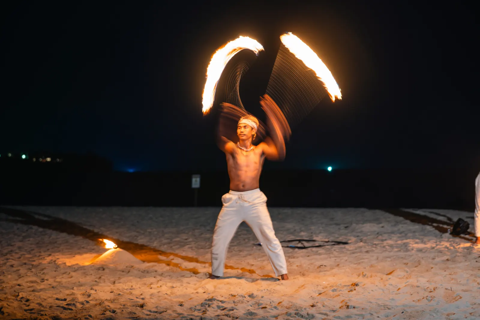 A fire performer creating arcs of light on a beach at night